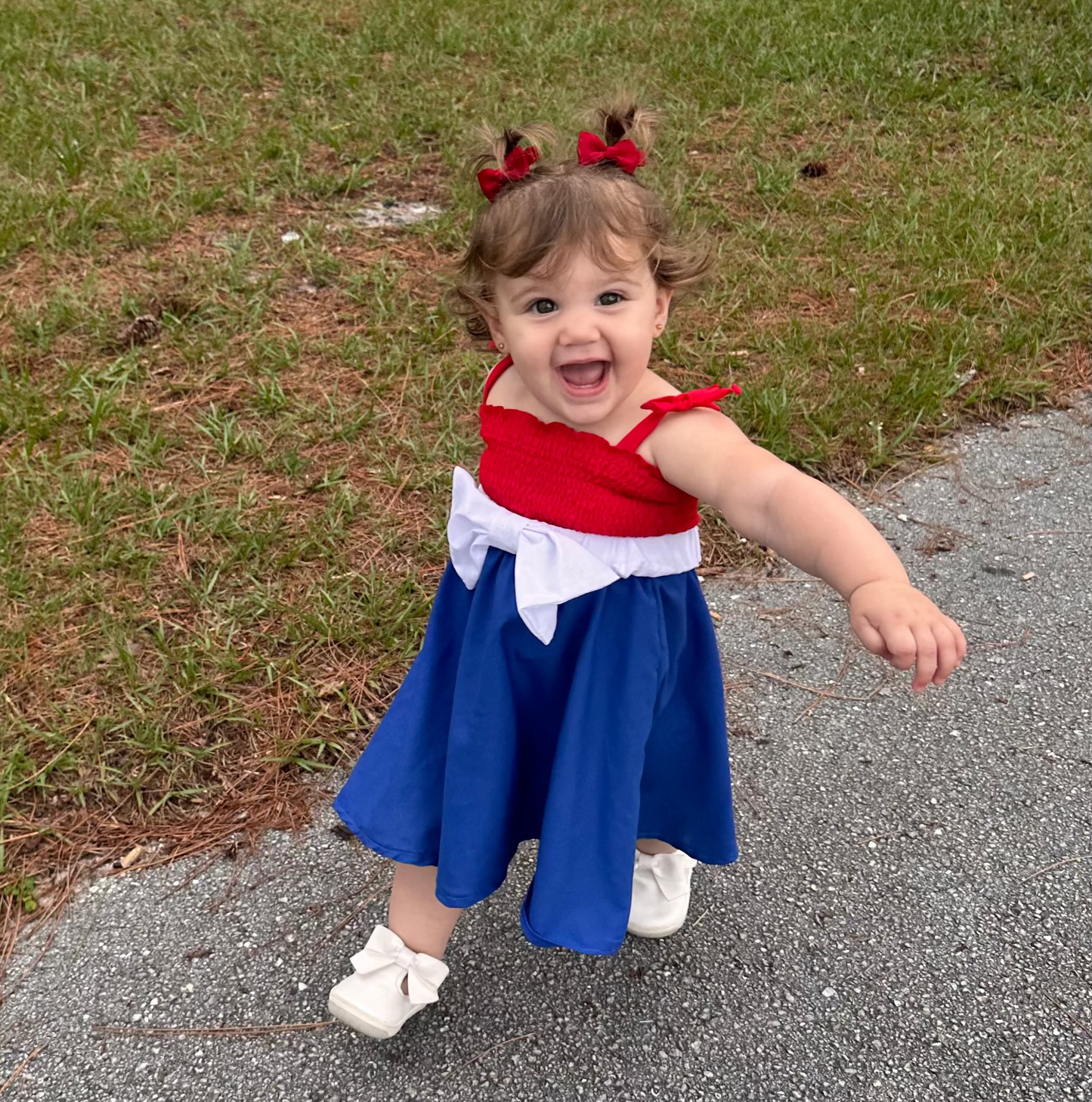 Child in a red and blue dress with white accents standing on a path in a park.