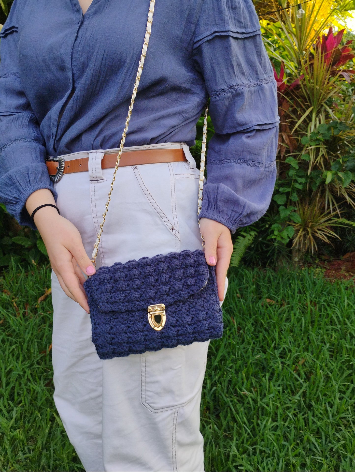 Person holding a blue crochet pouch outdoors with greenery in the background