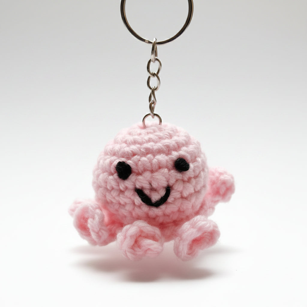 Pink crochet octopus keychain attached to a keyring with a blurred background