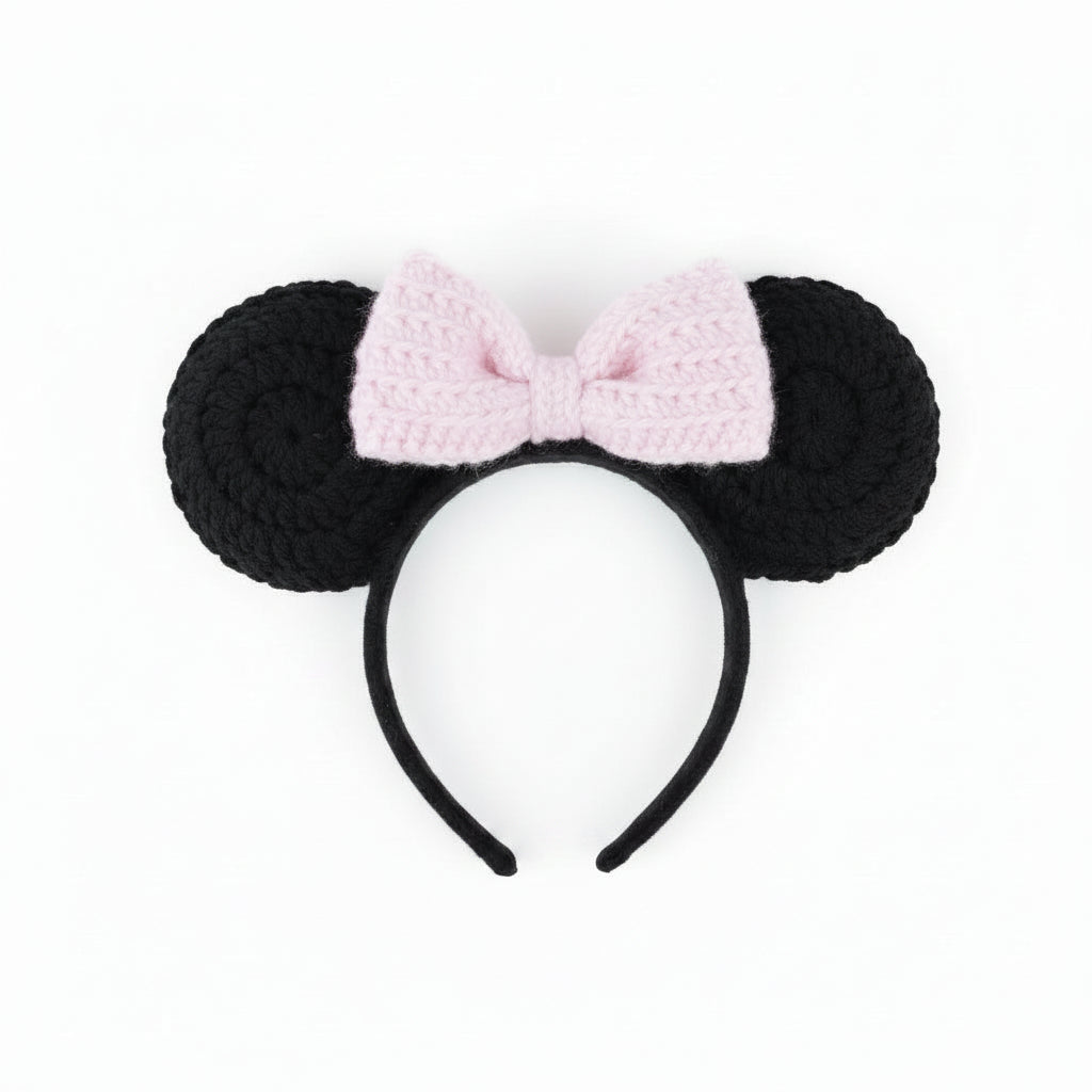 Handmade black mouse ears with a pink bow held over pebbles
