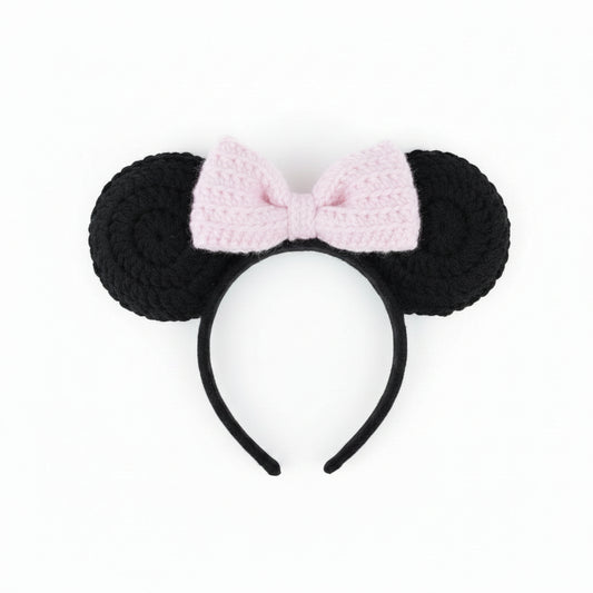 Handmade black mouse ears with a pink bow held over pebbles