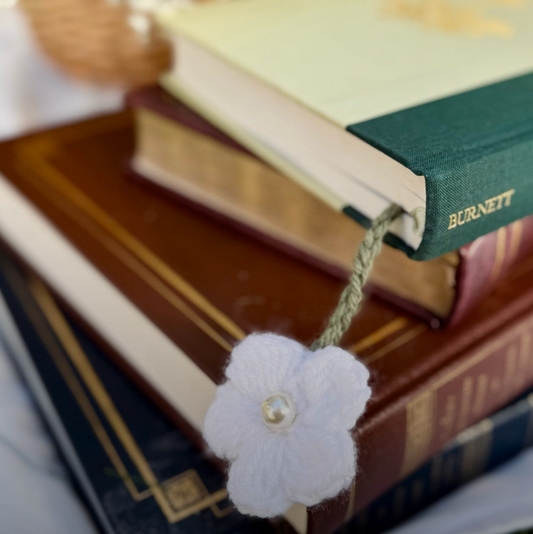 Stack of books with a white flower bookmark on a blurred floral background