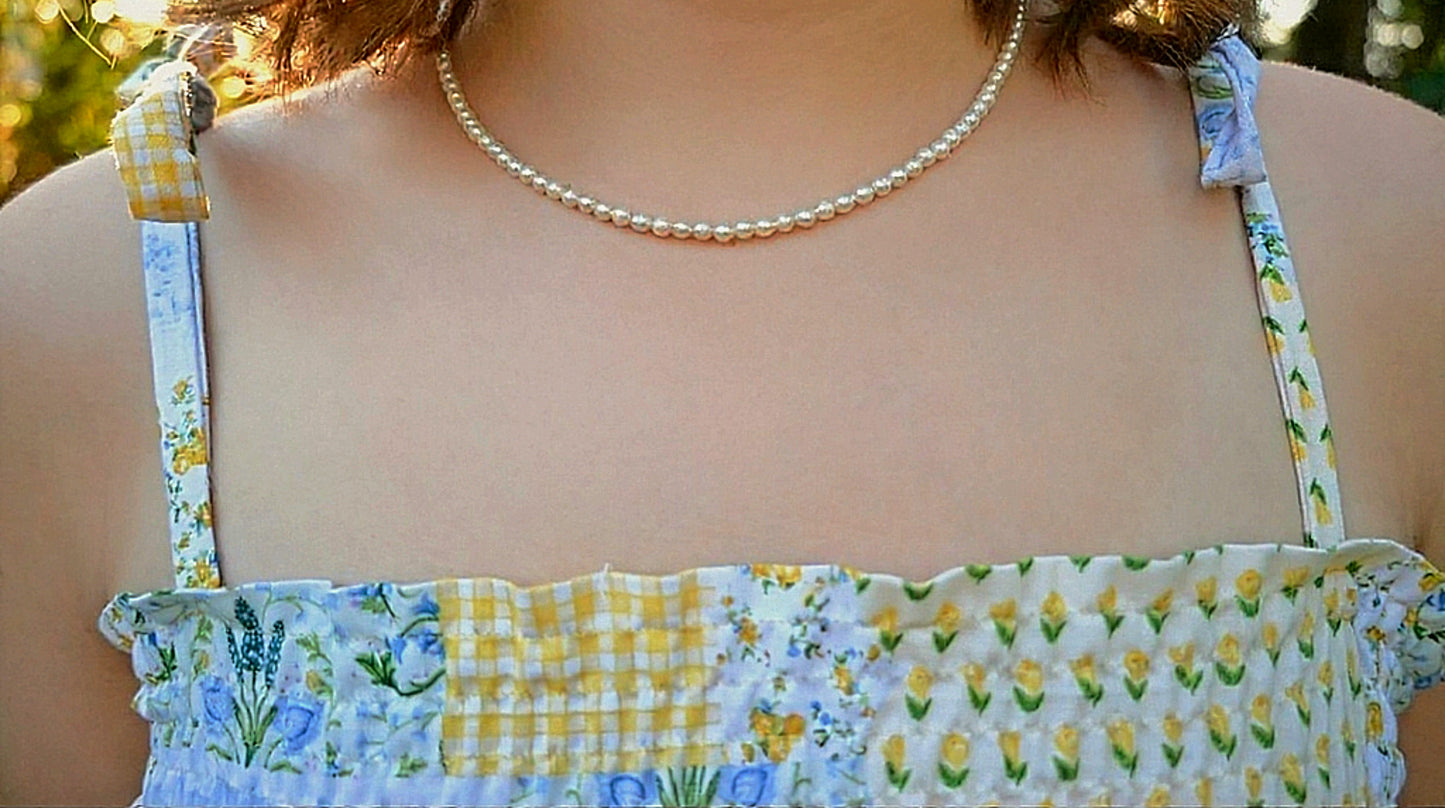 Close-up of a person wearing a floral dress with checkered straps and a pearl necklace.