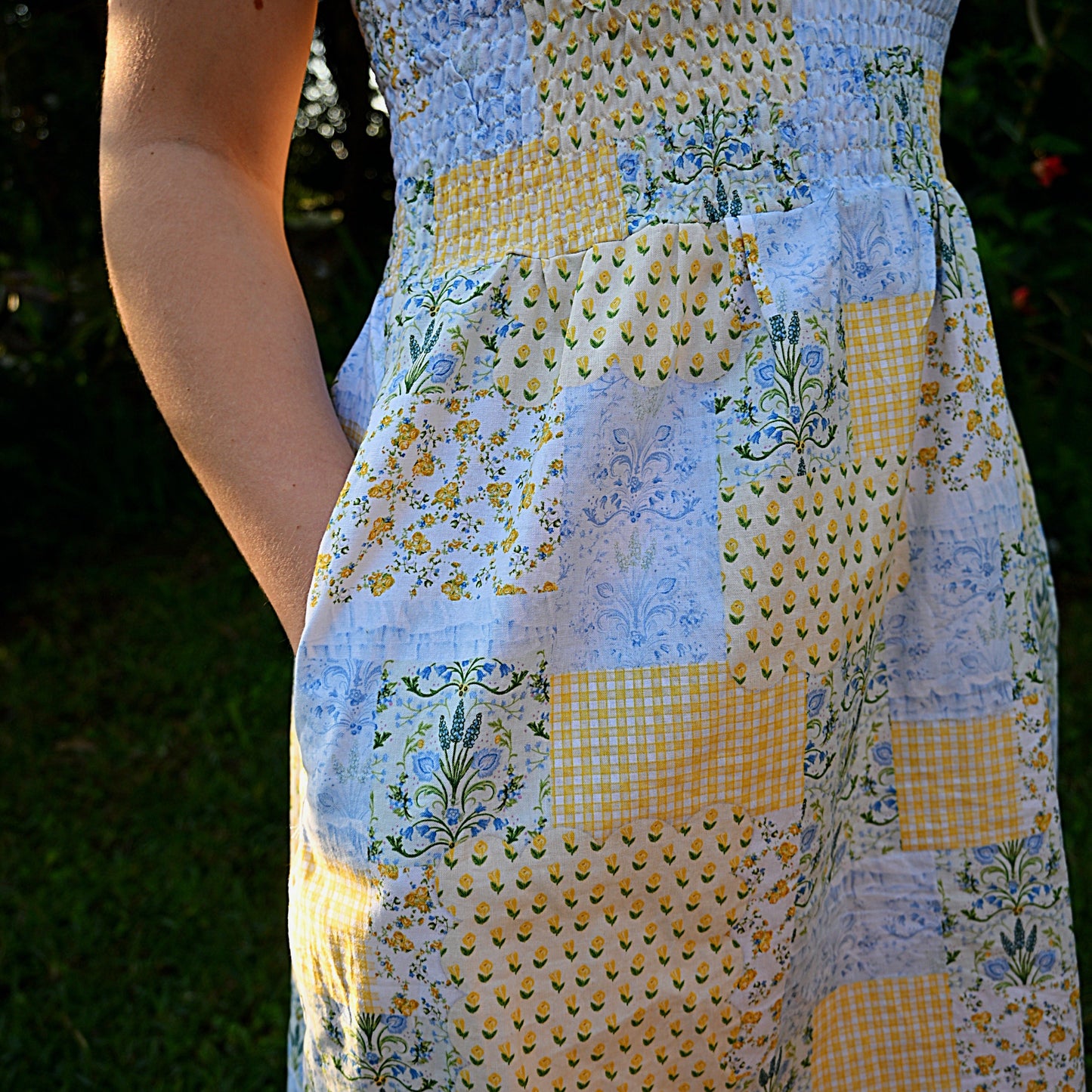 Person wearing a floral patchwork dress with a blurred natural background