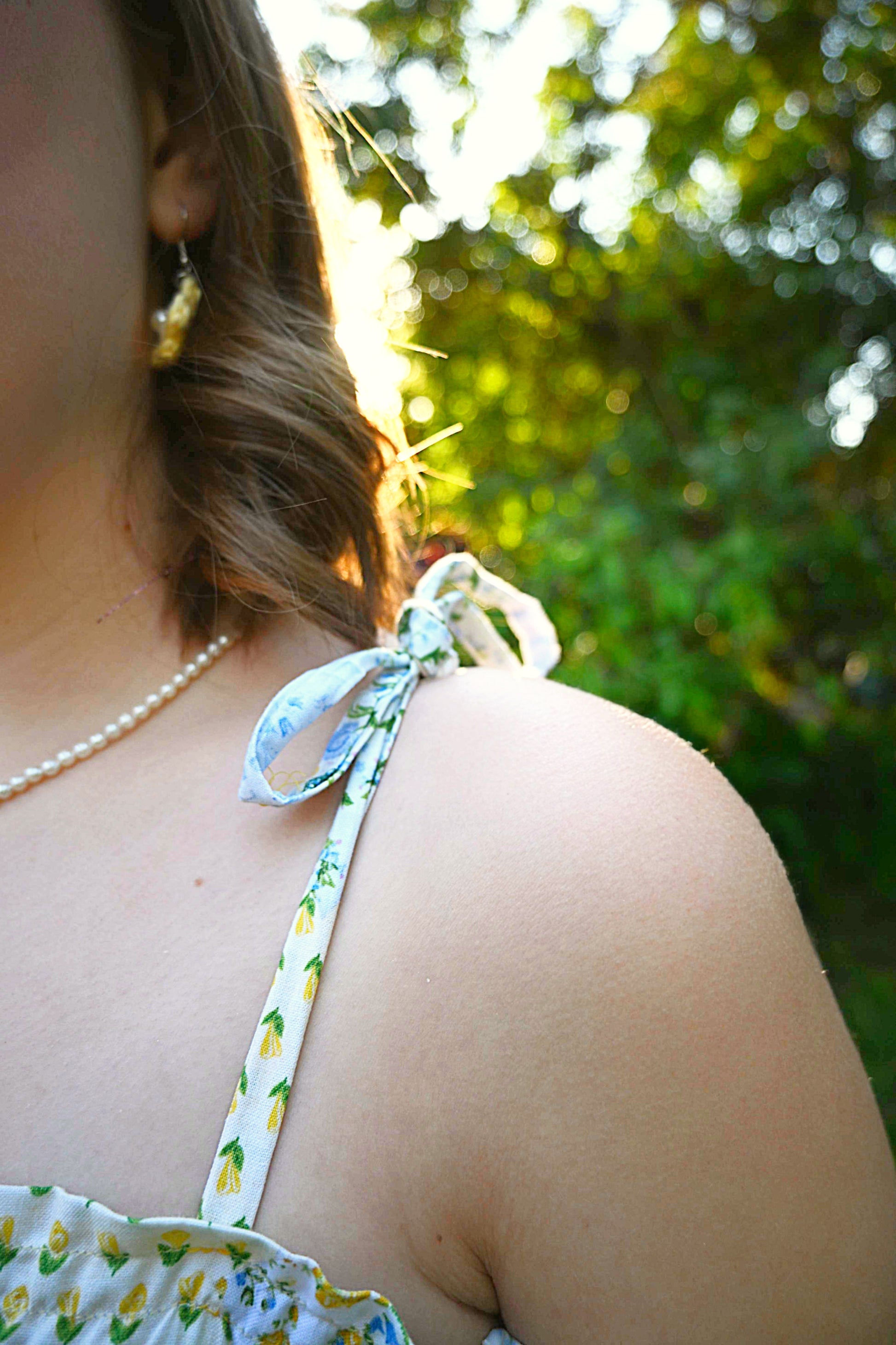 Close-up of a person wearing a floral top with a bow on an outdoor setting